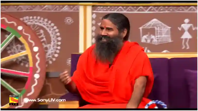 Baba Ramdev clapping his hands and laughing heartily on the couch of The Kapil Sharma Show, with host Kapil Sharma smiling next to him