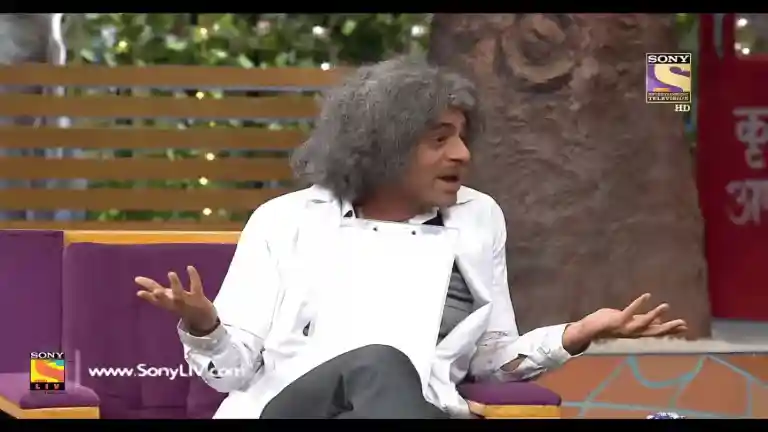 Dr Mashoor Gulati wearing a bright blazer, one hand raised dramatically, asking Kaisa laga mera mazak on The Kapil Sharma Show