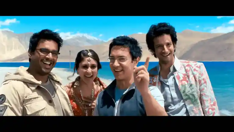 Rancho looking at Chatur with a knowing smile, Raju and Farhan beside him in the 3 Idiots classroom, the exact second the sarcastic line lands
